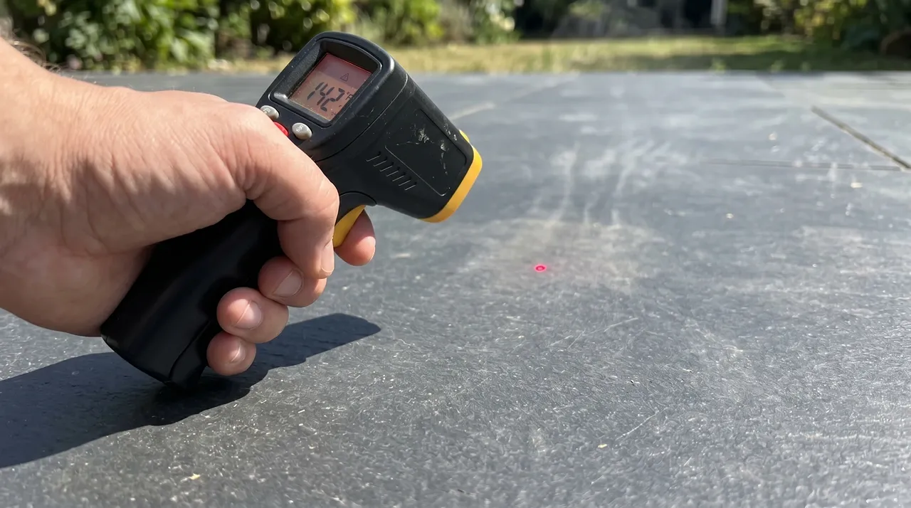 Infrared thermometer reading a dark patio slab at 142 degrees Fahrenheit in direct sunlight