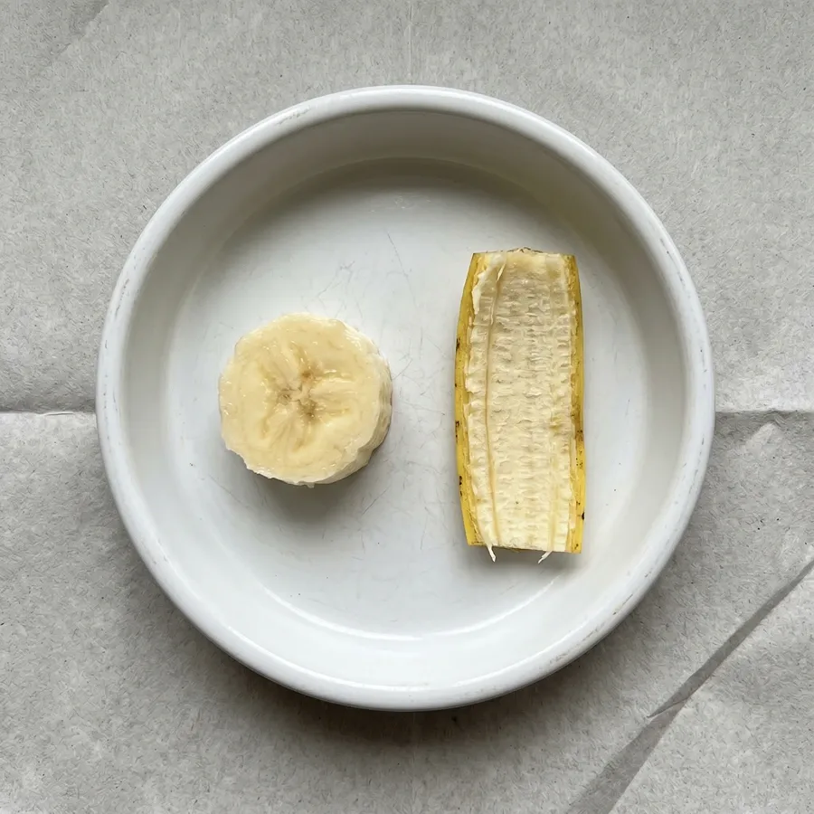 A peeled banana slice next to a chopped piece of banana peel in a feeding dish