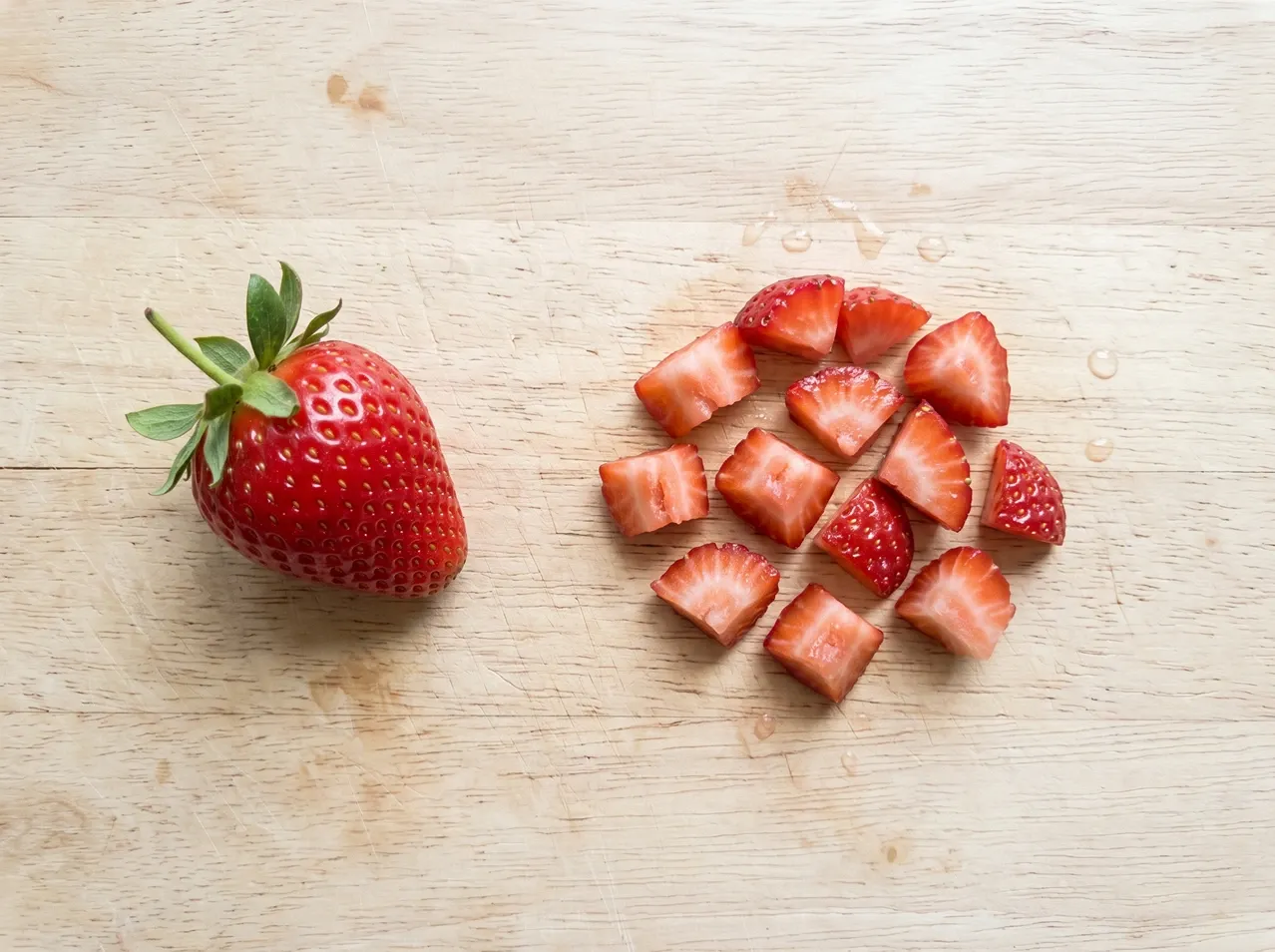 Whole strawberry next to small chopped strawberry pieces on a wooden cutting board